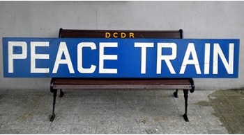 image shows a sign which reads Preace Train positioned on a bench at a train station