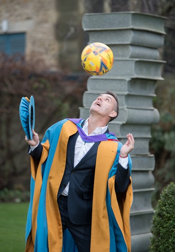 a picture of John Herdman dressed in graduation robes and heading a football