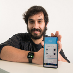Senior research assistant Luís Carvalho pictured wearing the Cue Band device on his wrist and holding a mobile phone with the Cue Band app open on the screen