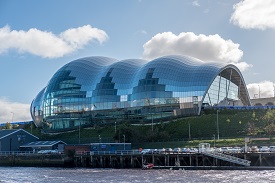 a large long train on a steel track with Sage Gateshead in the background