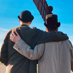 an image of two men, their arms around each others shoulders and backs to the camera, the angel of the north in the background