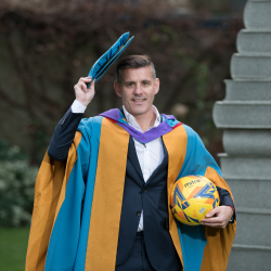 a picture of John Herdman dressed in graduation robes and holding a football