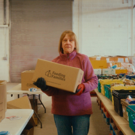 Feeding Families volunteer holding a box in the warehouse