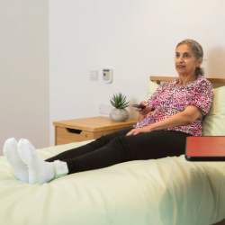 an elderly lady sits in a bed, she is wearing a smartsock on her left foot which has a sensor embedded in it