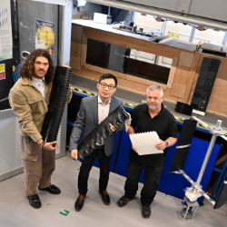 three man standing in front of a wind tunnel holding prototype parts of a wind turbine blade