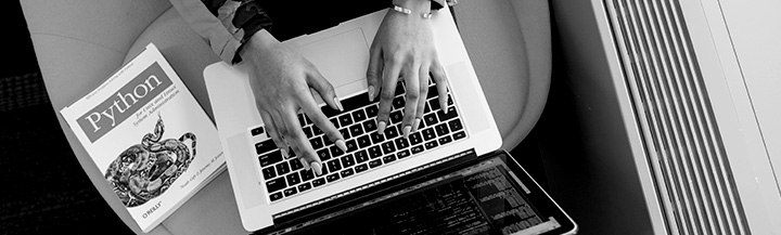 Hands typing on keyboard, next to a manual on Python