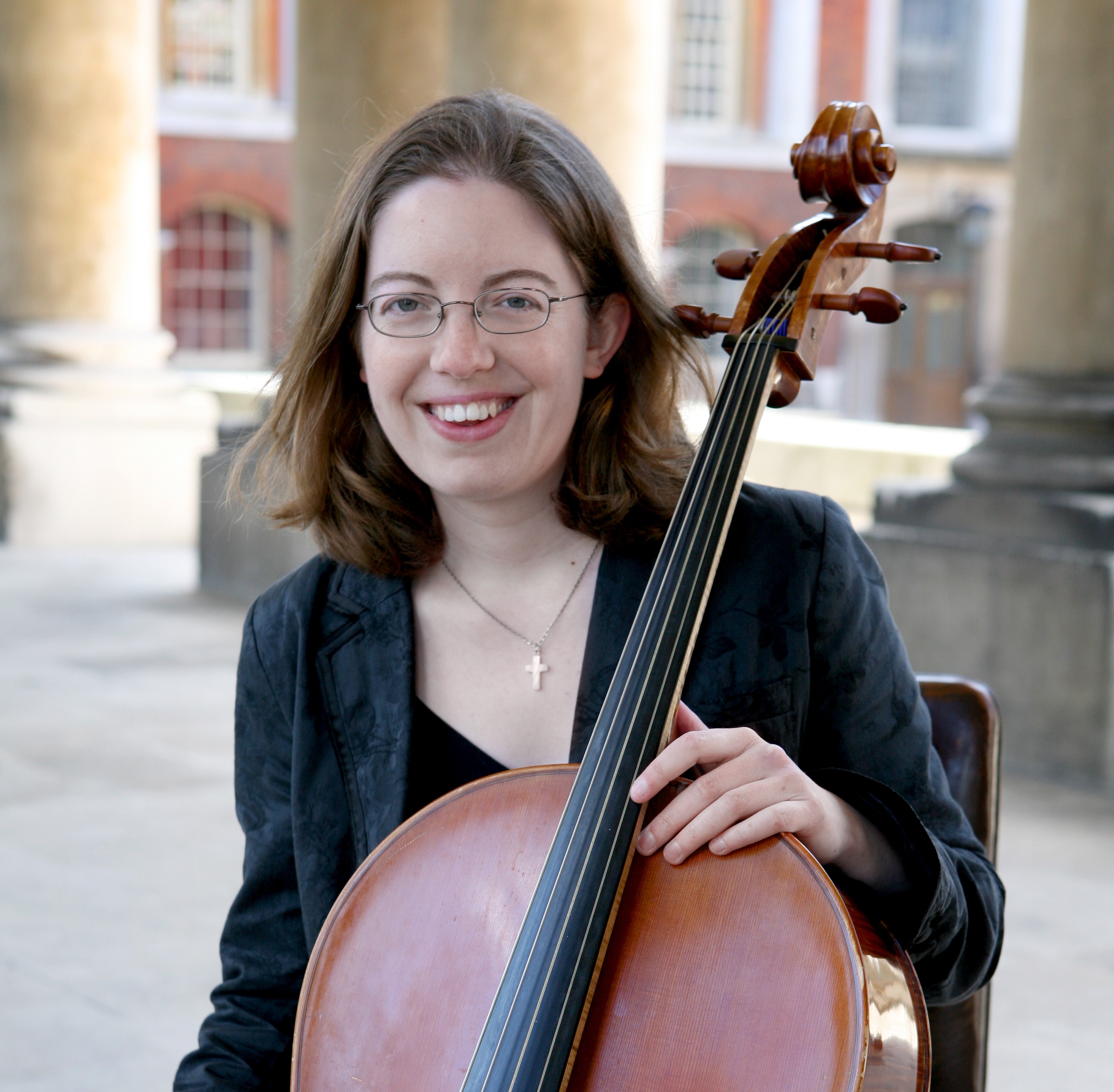 lady with brown hair and glasses sat in an old building holding a cello