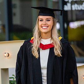 Image of student smiling wearing a graduation grown and cap