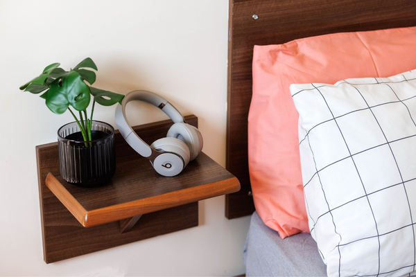 Close up of a bed side table with head phones and plant on top. 