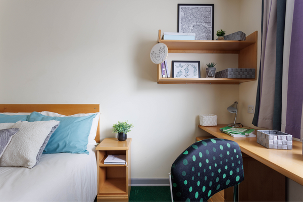 Student bedroom with bed, side table, desk, chair and shelves. 