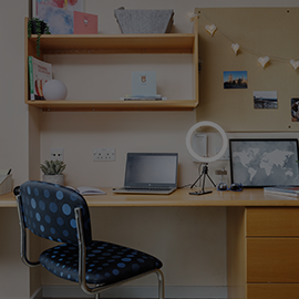 Image of a decorated bedroom displaying a desk, chair and shelves.