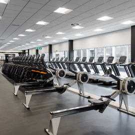 Gym with cardio equipment lined up against a glass wall. 