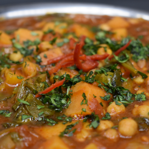 A close up image of a chickpea curry. The dish is garnished fresh coriander and chilli. 