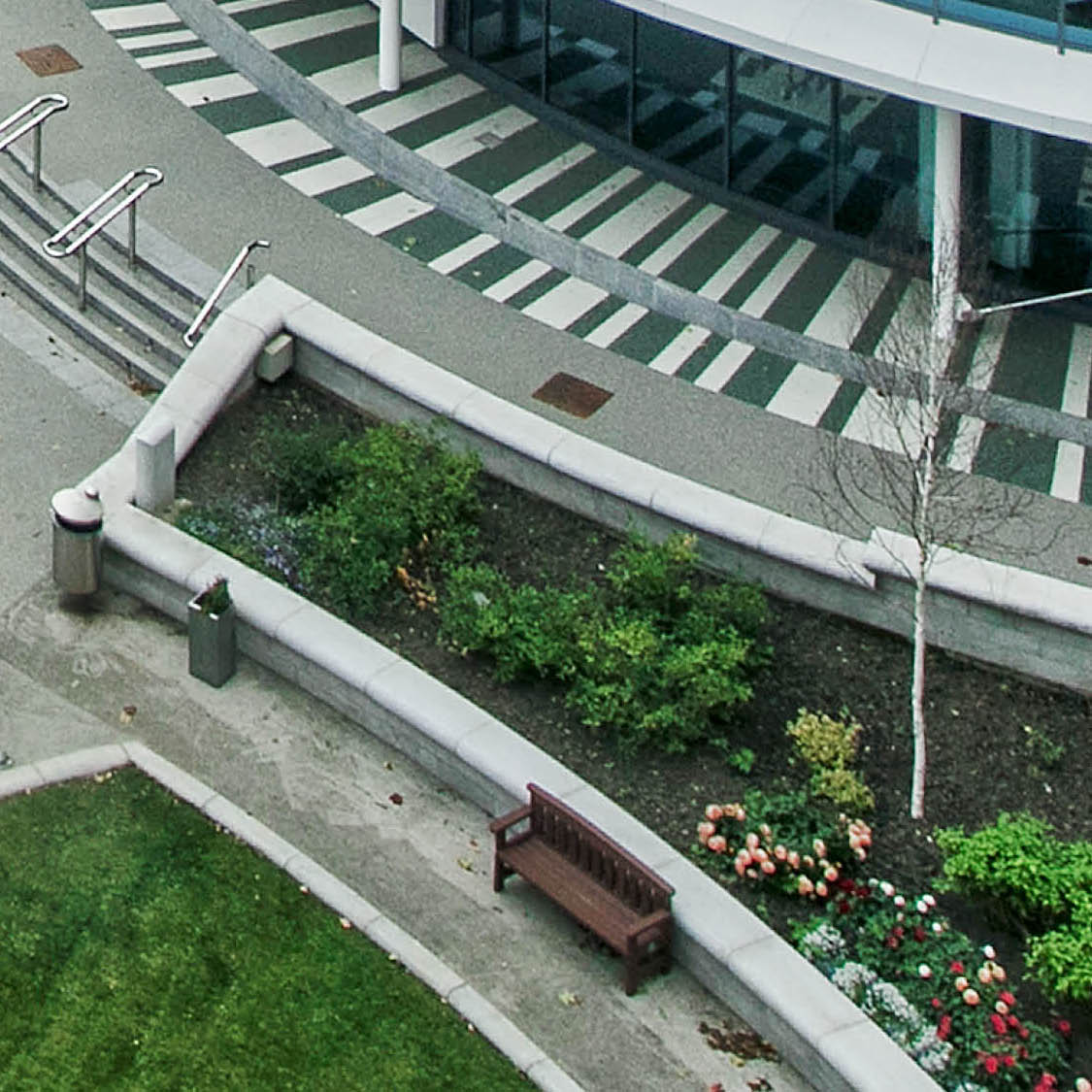 Ariel shot of a bench, lawn and flower bed surrounded by concrete paths.