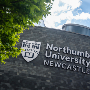 Photo of building with Northumbria University Logo, framed by green leaves. 