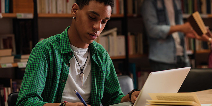 Male sitting at a laptop at a desk and writing