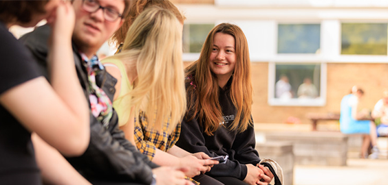 Group of students sitting together outdoors on campus, smiling and chatting