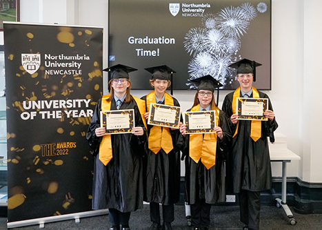 Four children in graduation gowns holding diplomas