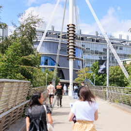 Students and pedestrians walking across a footbridge towards Northumbria University's campus buildings