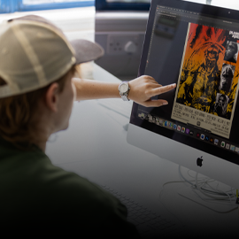 student pointing to a orange and yellow graphic poster on a desktop computer screen.