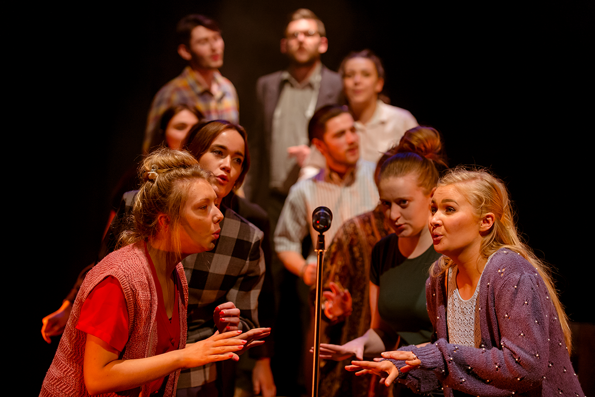 A group of students crowded around a microphone singing