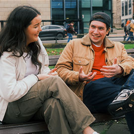 male student sitting on bench engaging in conversation with female student in newcastle city centre