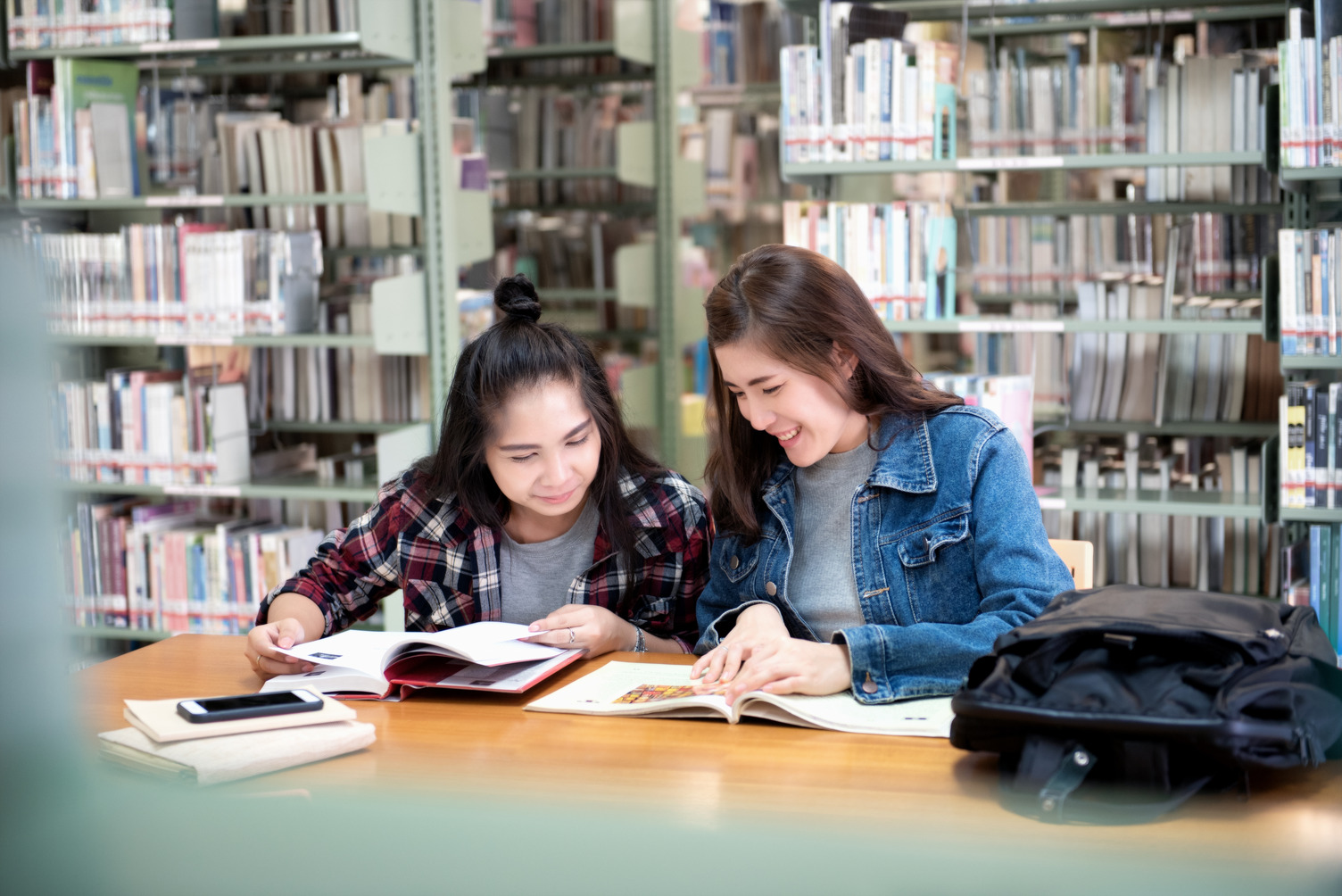 Two girl sat at a desk reading books in the library