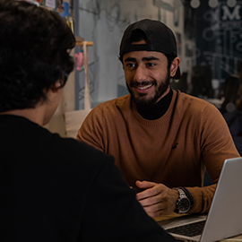 Student talking to another student, smiling with laptop in front of them