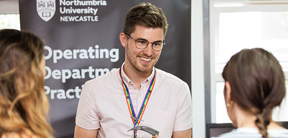 Man standing in front of sign that says "Operating Department Practice" at open day talking to two women and smiling