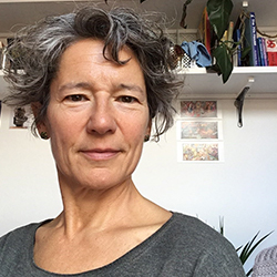 A woman with short grey curly hair wearing a grey top. 