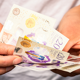 a pair of hands sorting through 5 £20 notes