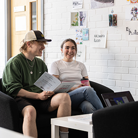 Two students sat on a sofa socialising and laughing together 