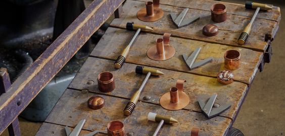 An assortment of handcrafted metalwork pieces displayed on a weathered wooden cart with purple-painted rails and a visible wheel.