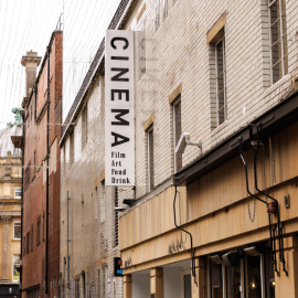 Looking down an alley where a large white sign is attached to a building. It reads 'Cinema'