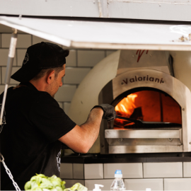 A chef reaching into a burning pizza oven