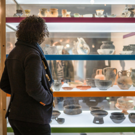 A woman stands before a glass museum cabinet filled with artefacts