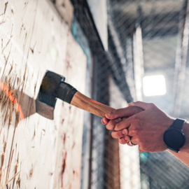 Two hands clasped around an axe handle, pulling it from a wooden board